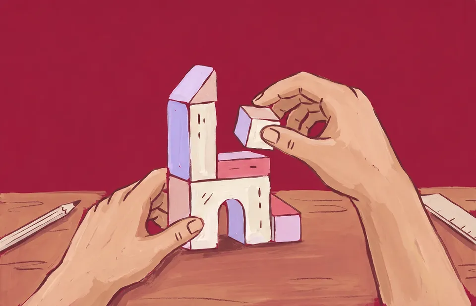 Hands stack paper and lavender toy blocks into a small tower on a cranberry ground
